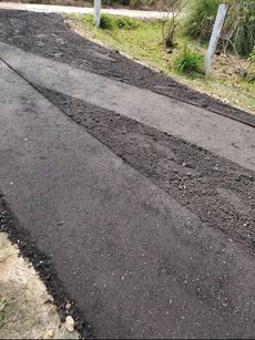 A path of dark, freshly laid asphalt with a strip of rougher gravel cutting across it, situated next to a grassy area.