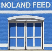 Blue building with white trim; "NOLAND FEED" sign above double doors.