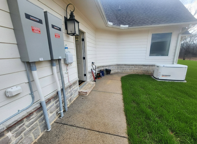Exterior of a white house with a paved walkway, electrical boxes, and a generator on the grass.