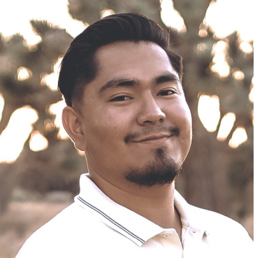 Man smiling in a white polo shirt outdoors with blurred trees in the background