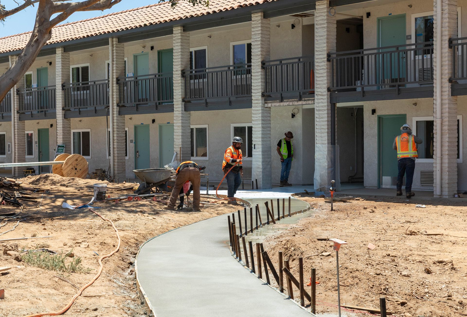 Workers in orange vests building a concrete walkway beside an apartment complex under construction