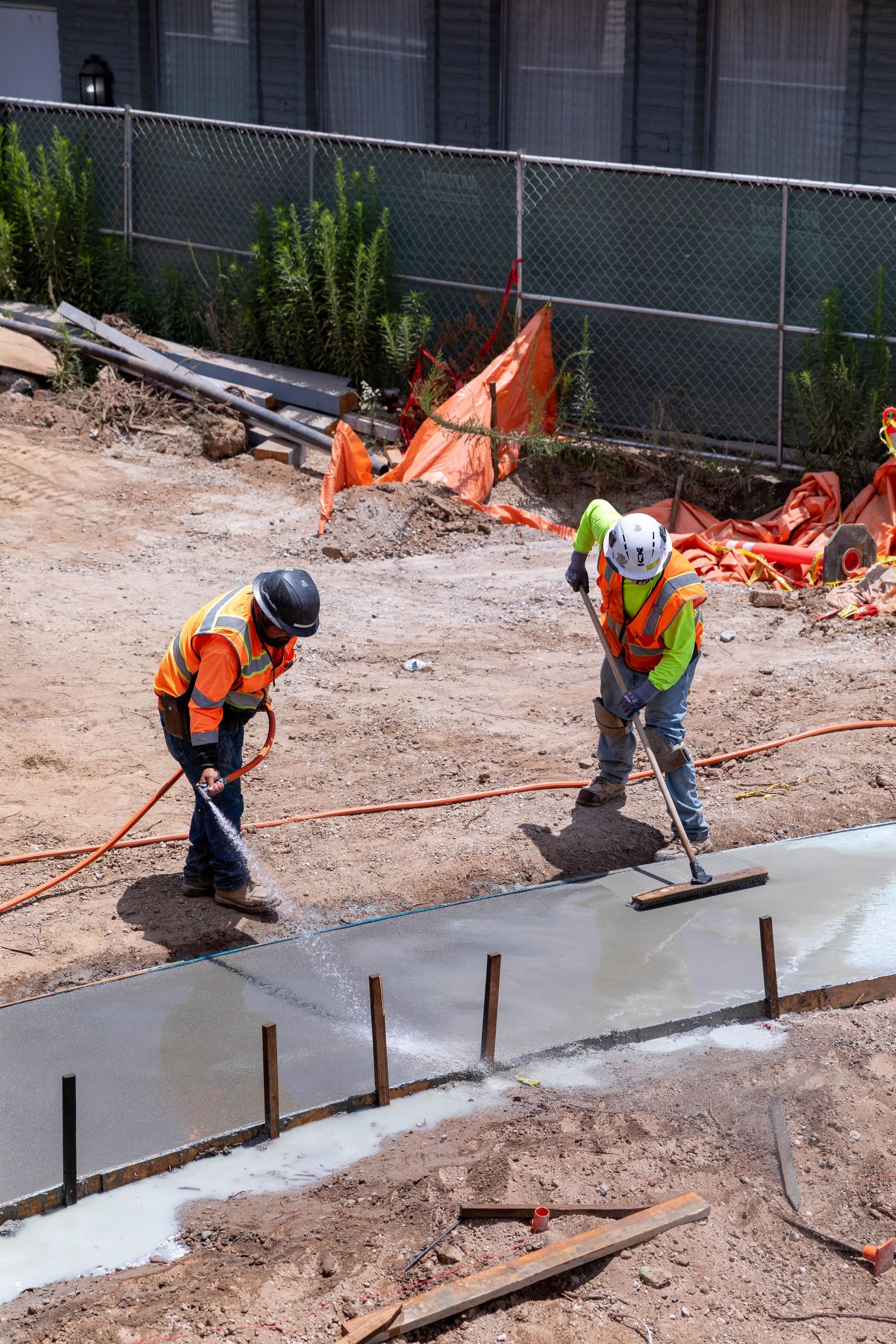 Construction workers smoothing wet concrete near orange safety fencing at a roadwork site