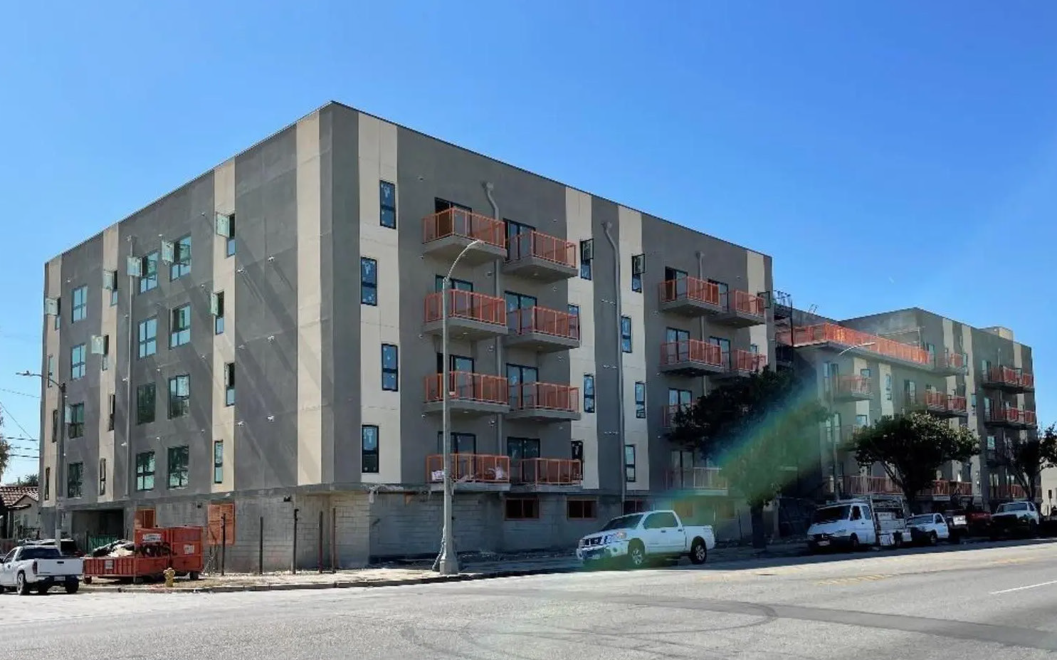Modern apartment building on a sunny street corner with parked cars and balconies