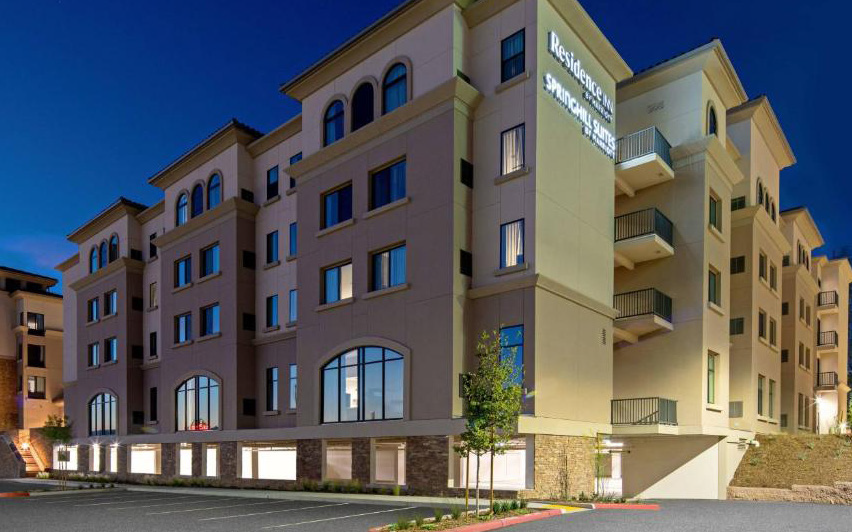 Modern apartment building at dusk with beige walls, arched windows, and lit ground-floor windows