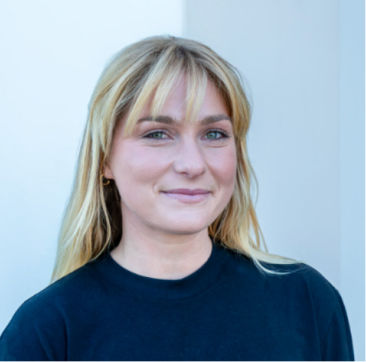 Portrait of a woman with blonde hair in a dark top against a light blue background