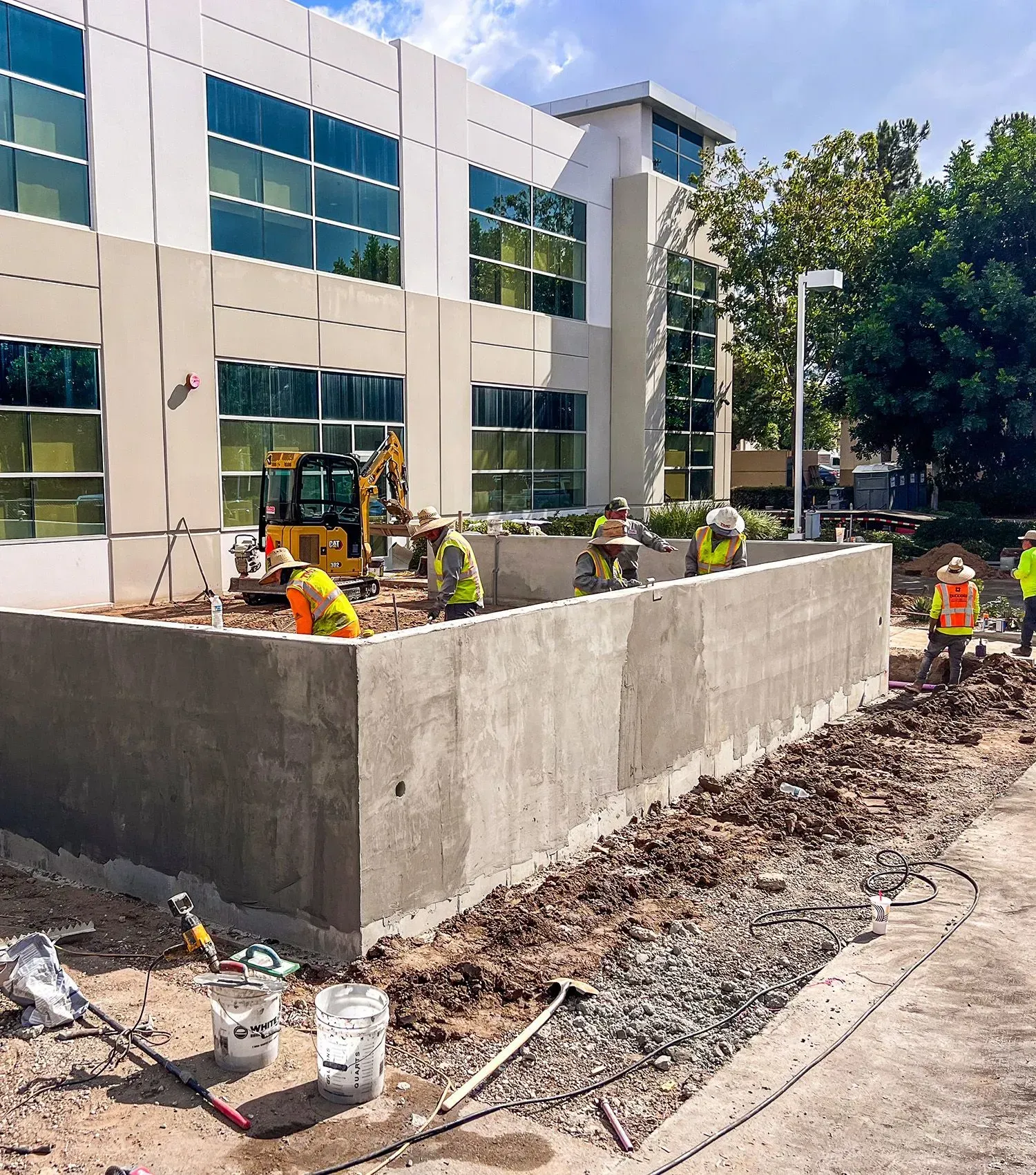 Construction workers building a concrete retaining wall outside a modern office building