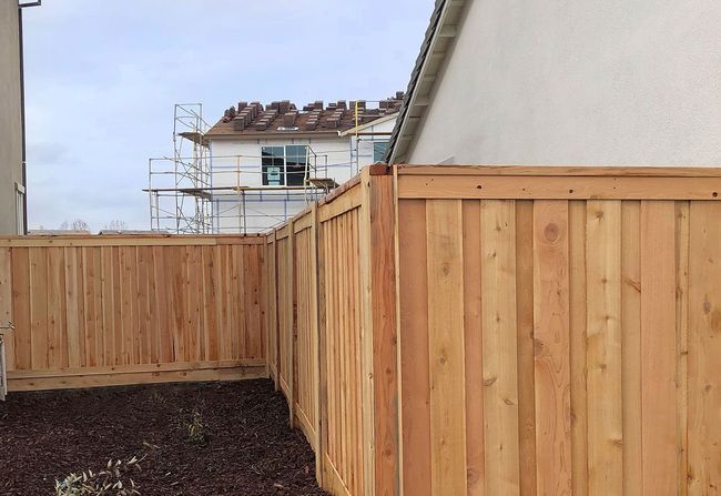 Wooden fence surrounds a yard with mulch, house under construction visible behind it.