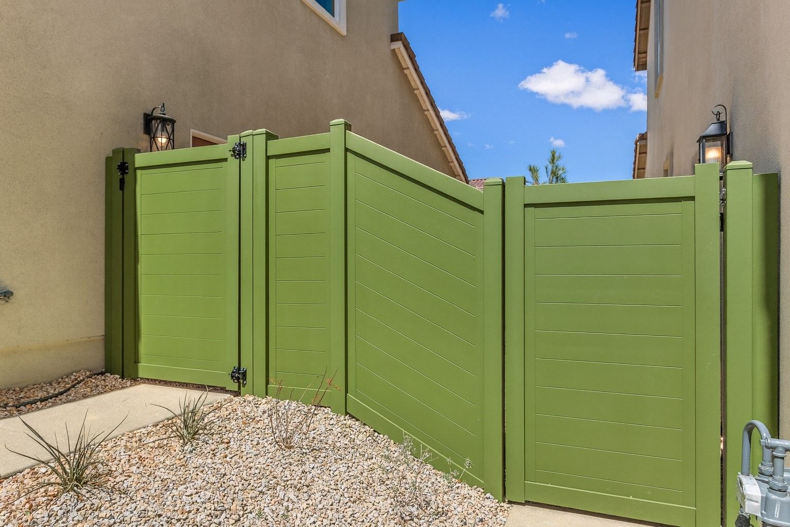 Wooden fence with decorative lattice top, bordering green lawn and gravel bed with tufted plants.