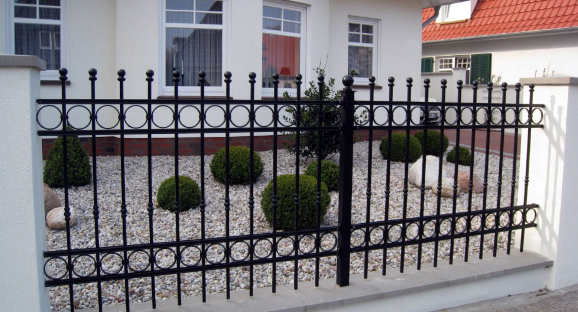 Black wrought iron fence with decorative circles and spikes, in front of a white house with landscaping.