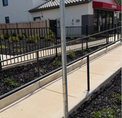 Concrete sidewalk ramp with black railings beside a building entrance and parking lot