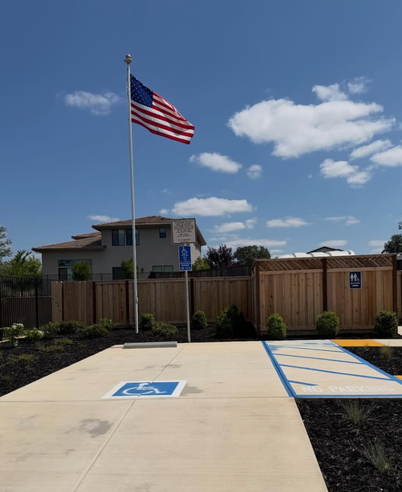 Parking lot with American flag, wooden fence, and accessible parking spaces under a blue sky.