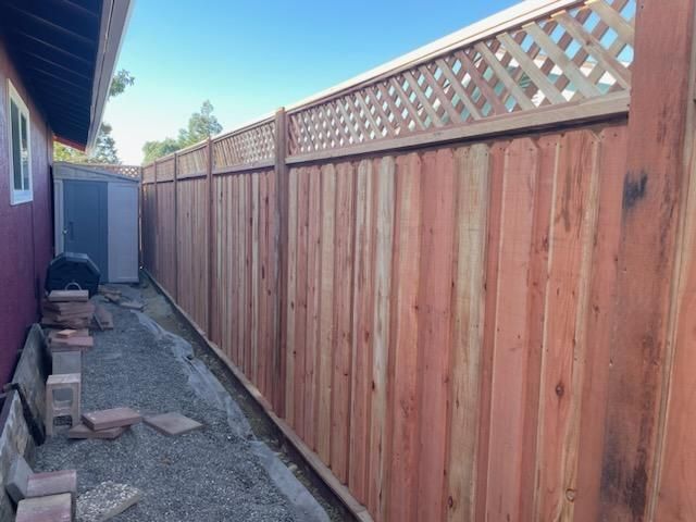 Narrow side yard with a long wooden fence, gravel path, and a gate beside a house.