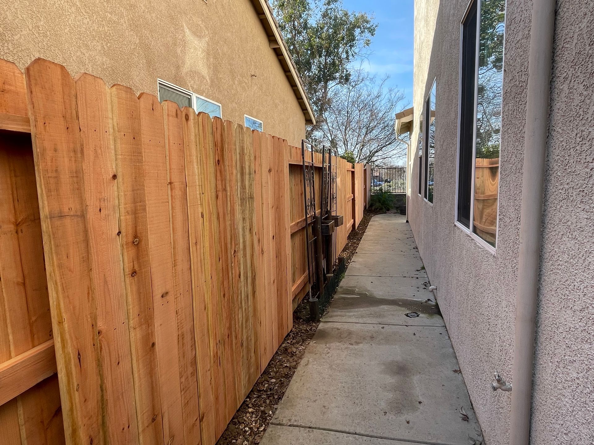 Tan vinyl fence in front of a yellow house with greenery.