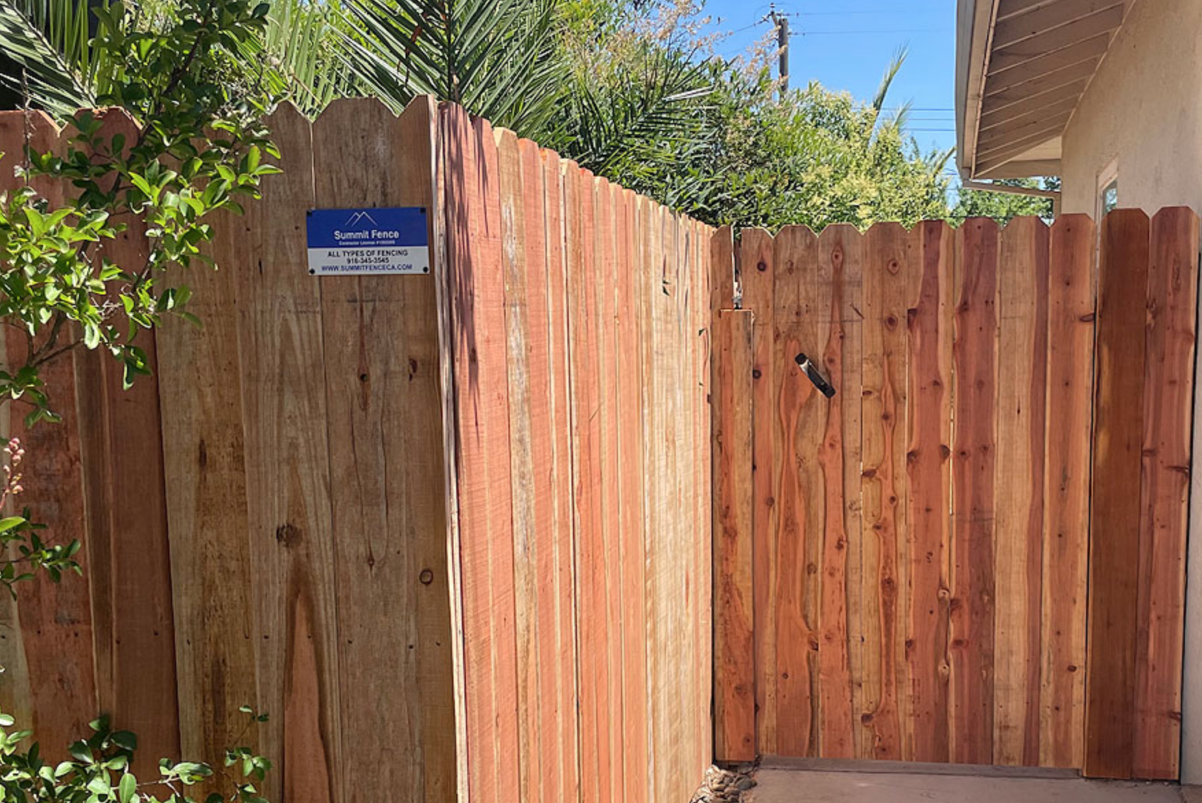 Wooden fence with a gate. The fence is made of vertical planks of wood in reddish-brown tones. A security sign is attached.