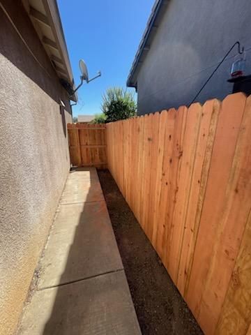Narrow side yard with concrete path, tan stucco wall, and tall wooden fence under a blue sky