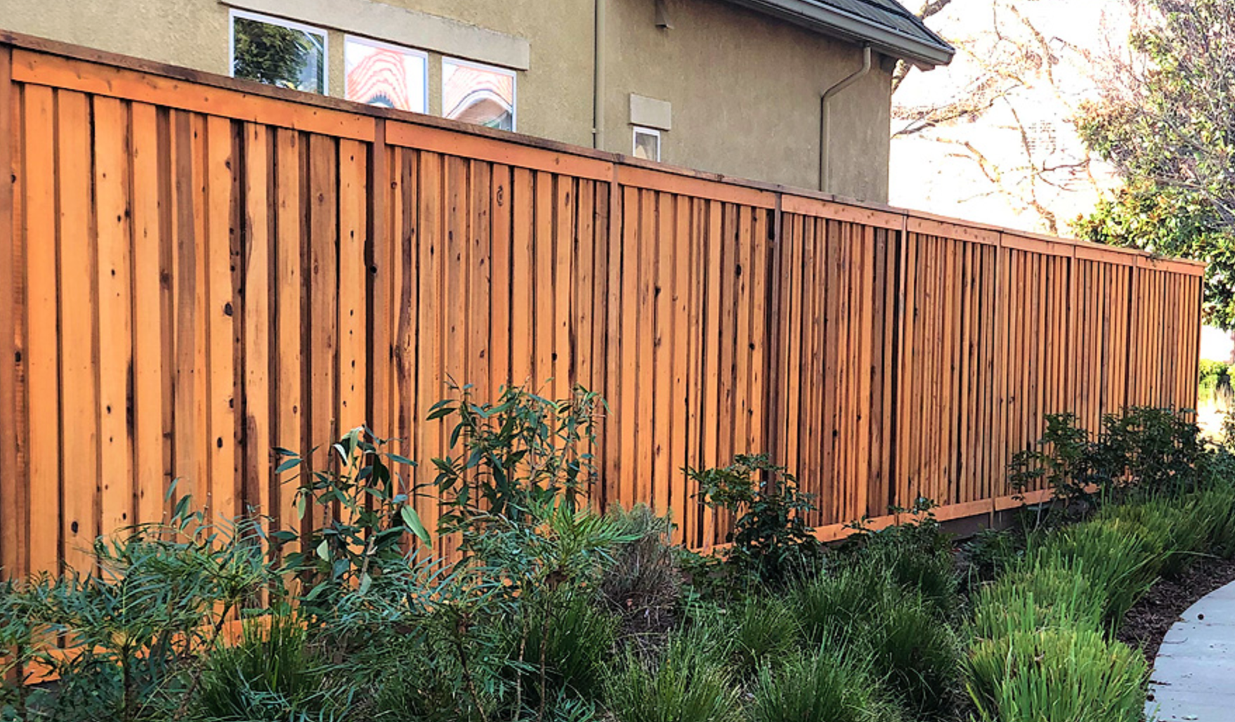 Wooden fence with landscaping against a beige house.