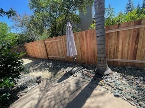 Backyard patio with wooden fence, stone border, palm tree, and closed patio umbrella in sunlight