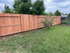 Freshly installed wooden fence bordering a grassy backyard with a small tree and cloudy sky