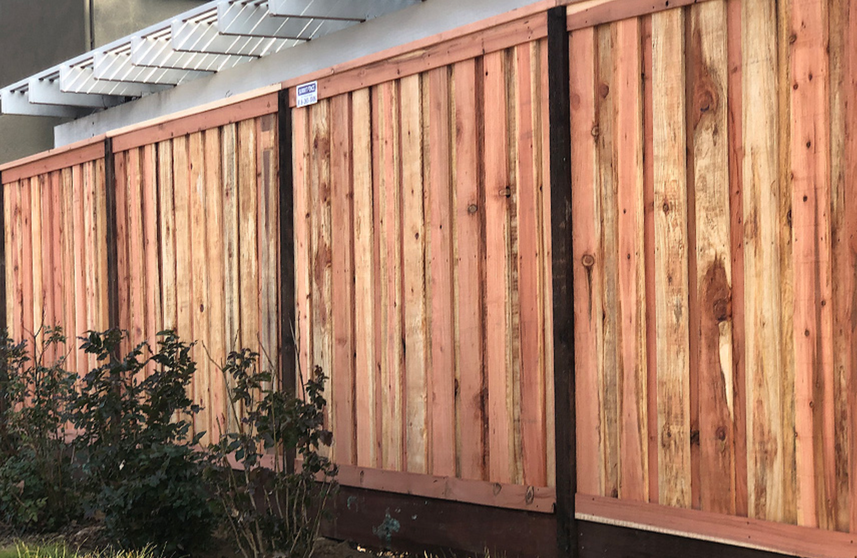 Wooden privacy fence with vertical planks, brown and tan, near a building.