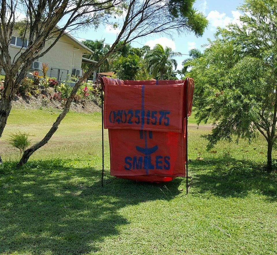Red Signboard with Blue Smiles Text in A Grassy Yard, Near a House and Trees — Green Waste in Thuringowa Central, QLD