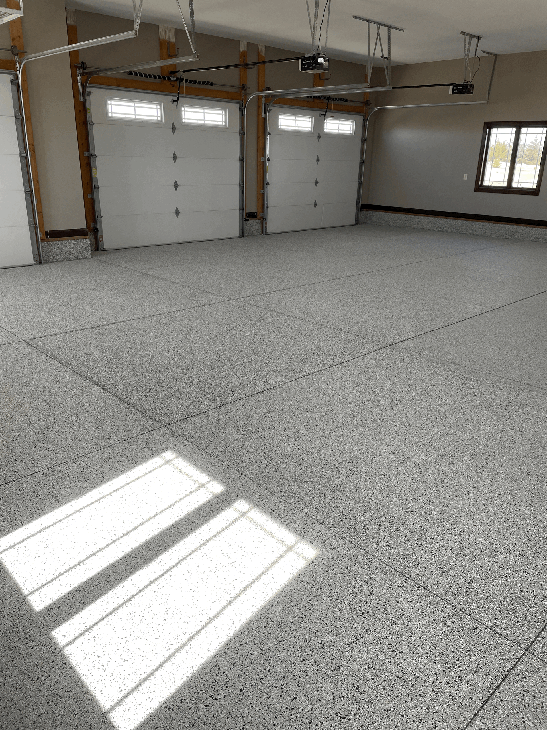 An empty garage with a grey speckled epoxy floor and two white garage doors.