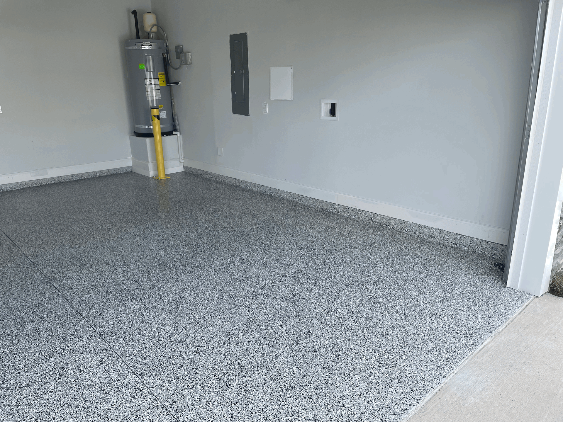 A garage interior featuring a gray speckled epoxy floor, a water heater on a concrete stand, and light gray walls.