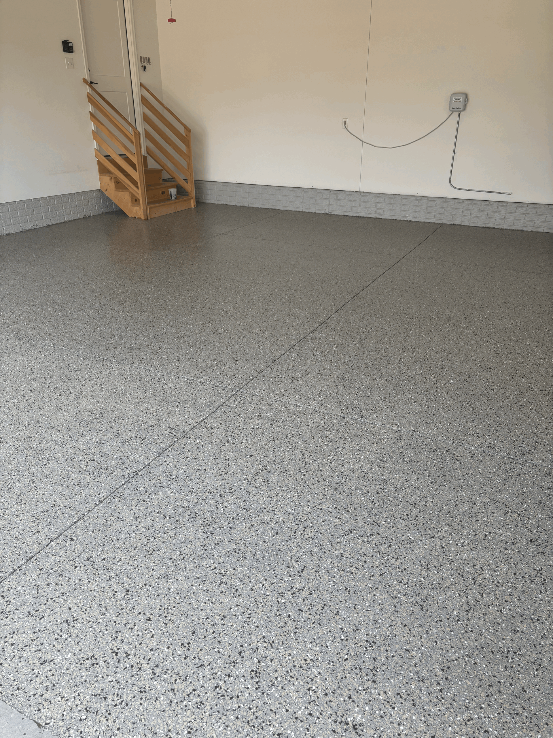 A room featuring a freshly installed, light gray epoxy floor with black and white speckled chips and matching baseboards.