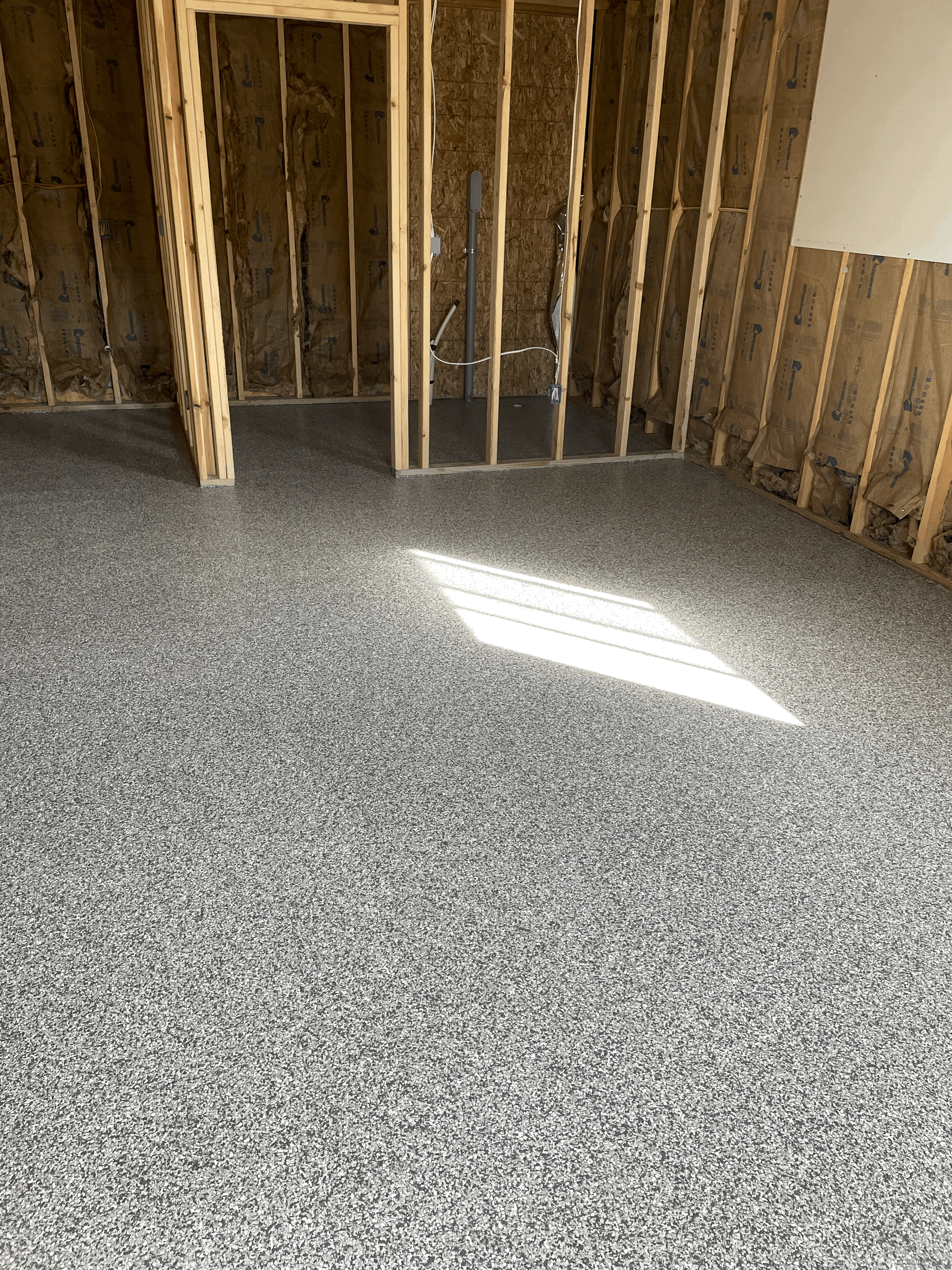 A newly installed grey and white speckled epoxy floor in a room with unfinished wooden wall studs.