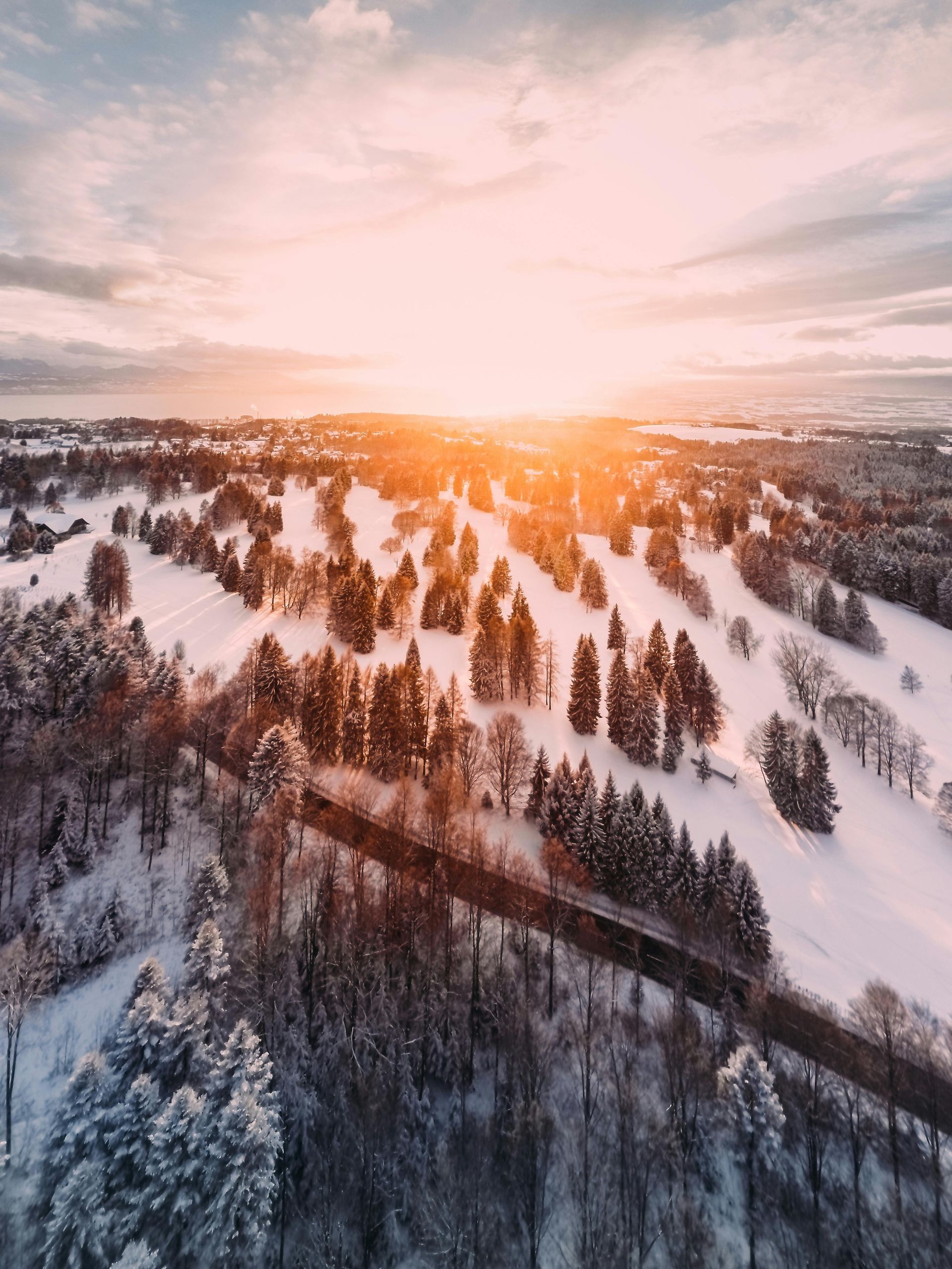 Encosta nevada com árvores dispersas, uma estrada e um pôr do sol quente.