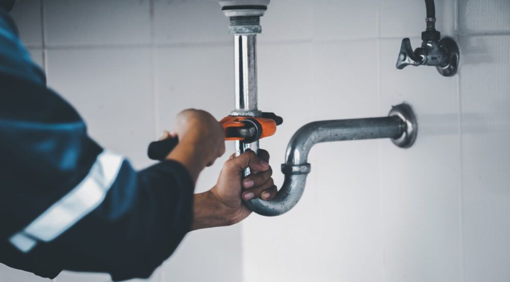 A plumber is fixing a sink pipe with a wrench.