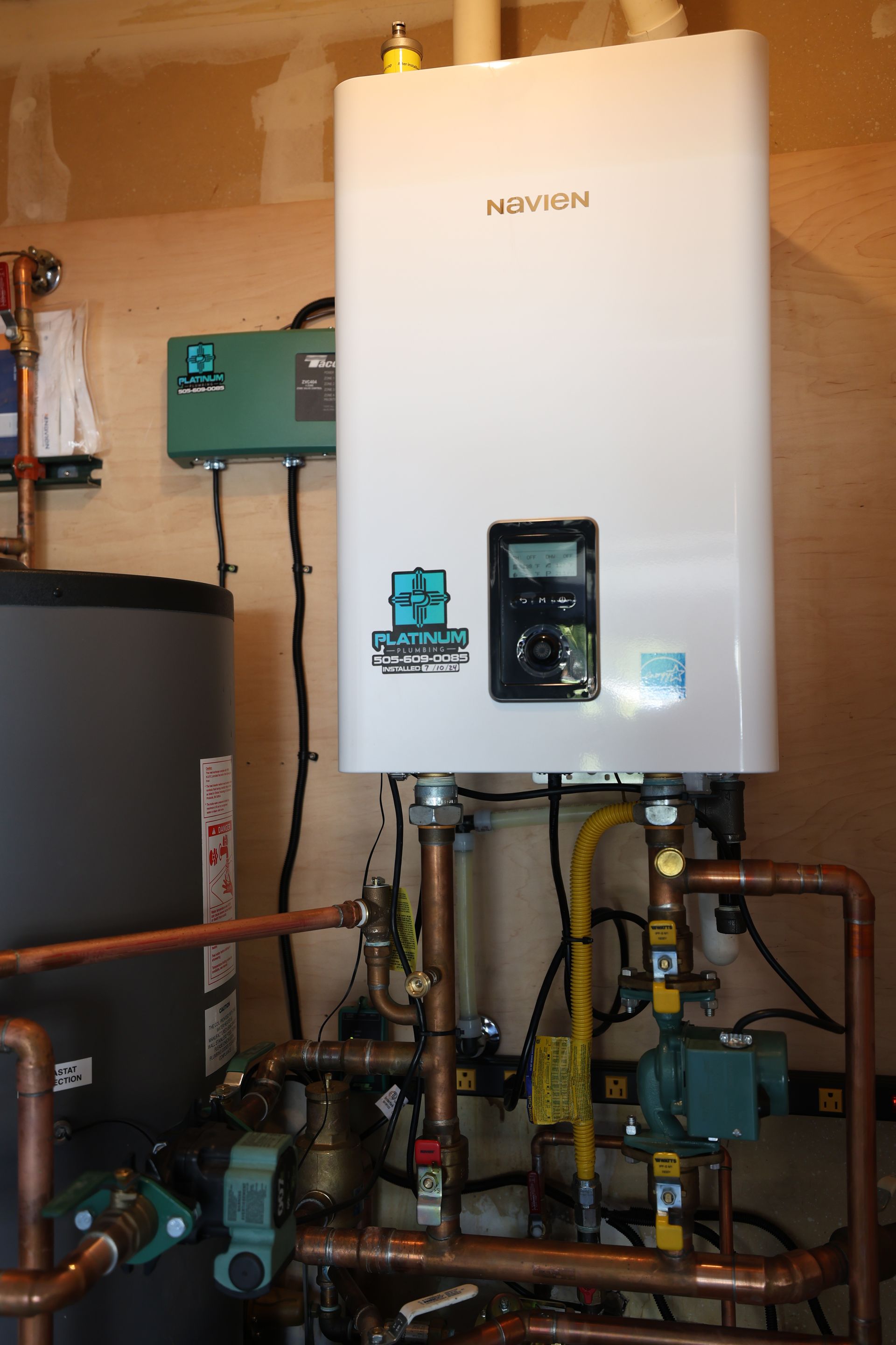 A white water heater is surrounded by copper pipes