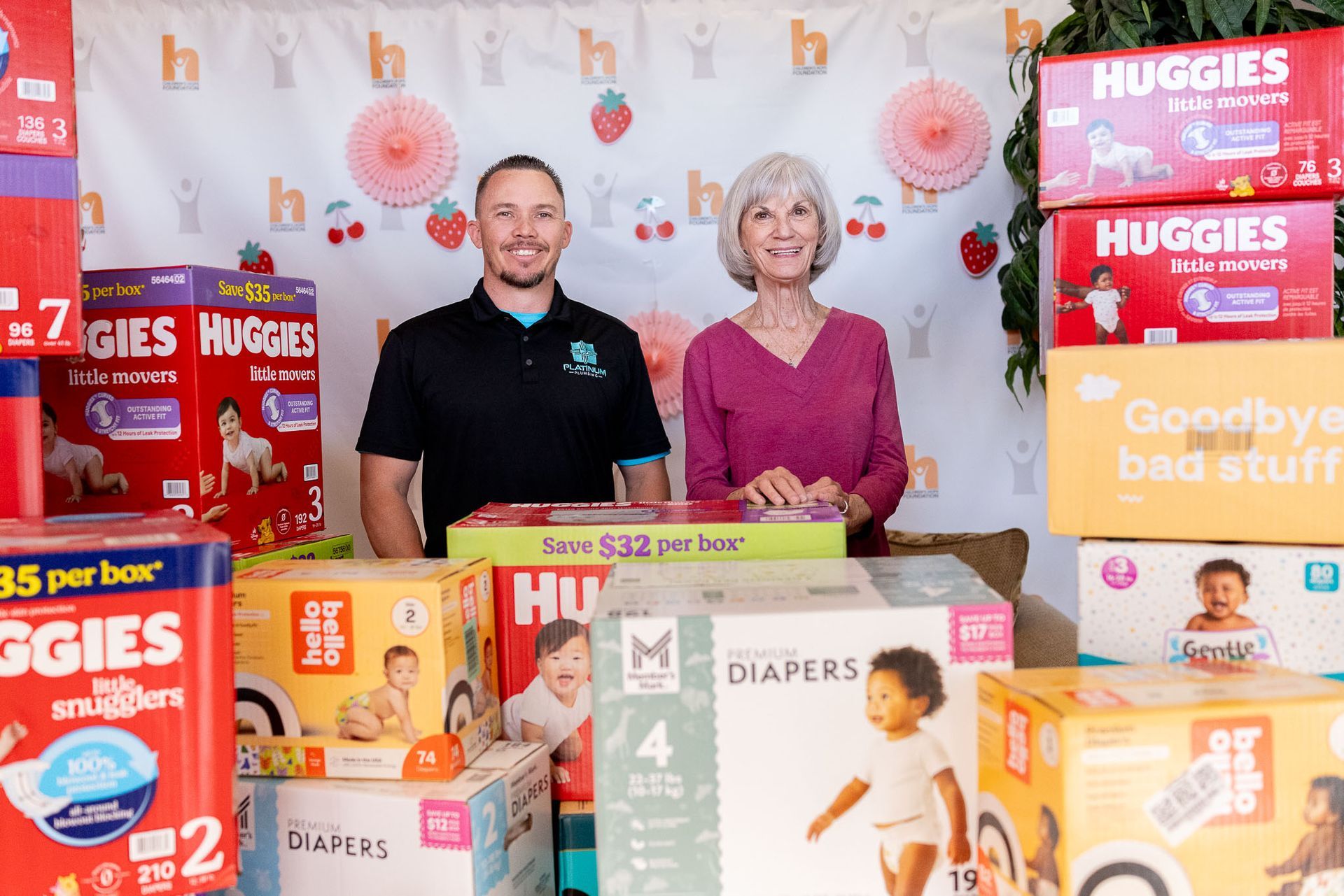 Two people behind stacked Huggies diaper boxes at a promotional display, smiling.