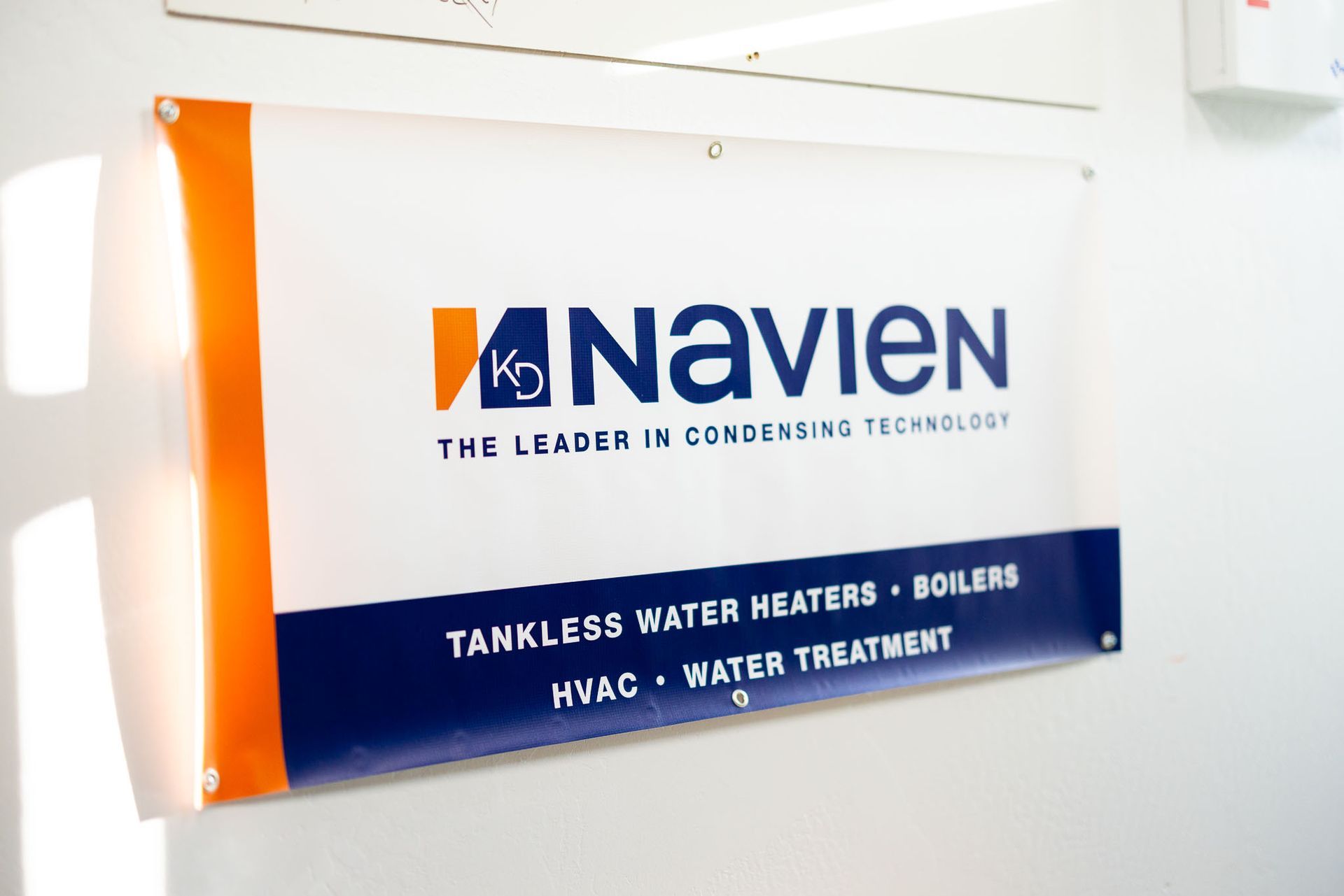 Navien banner on a white wall with blue and orange branding, listing tankless water heaters and boilers