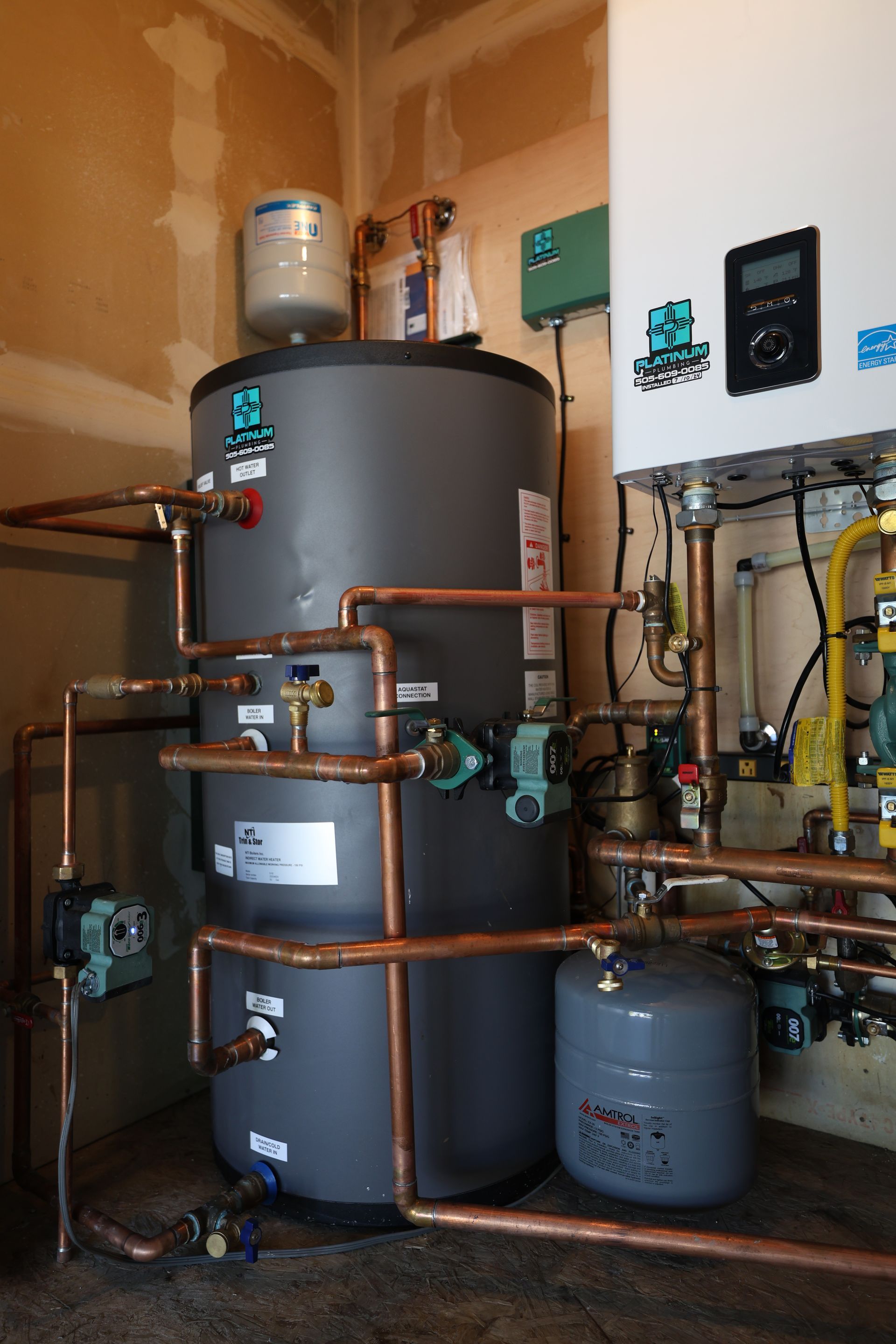 A water heater is sitting in a room surrounded by pipes.