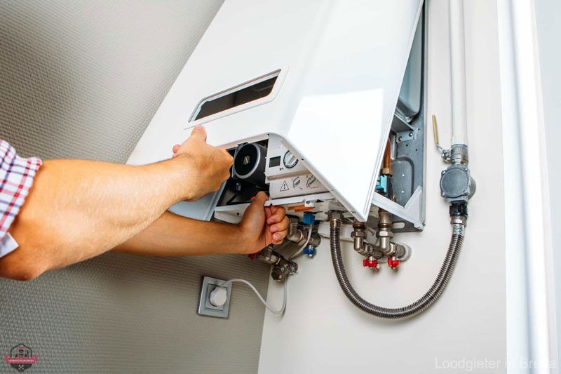 A man is fixing a water heater on the wall.
