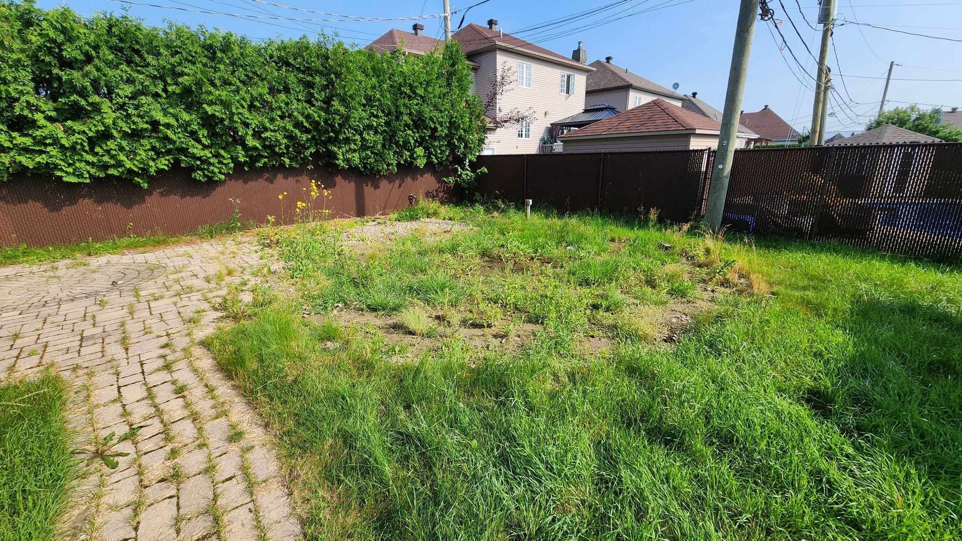 Une allée en briques menant à un champ herbeux avec une clôture en arrière-plan.