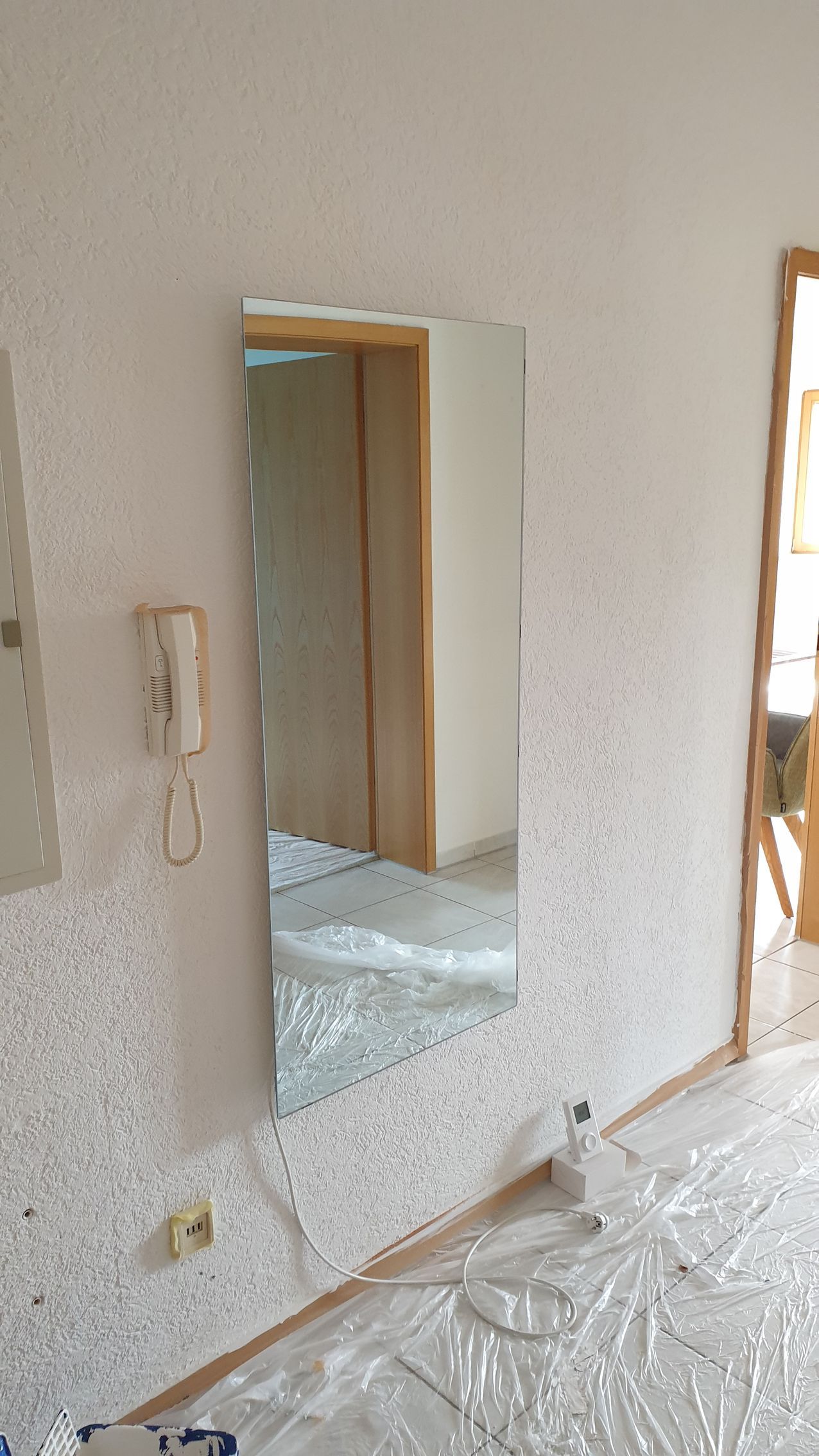 Teilweise renoviertes Zimmer mit verputzten Wänden, einer Türöffnung und Plastikfolie auf dem Boden.