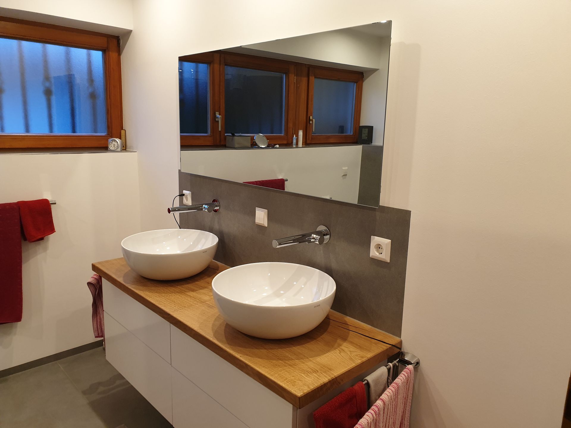 Moderner Badezimmerwaschtisch mit zwei weißen Aufsatzwaschbecken, großem Spiegel und Holzarbeitsplatte.