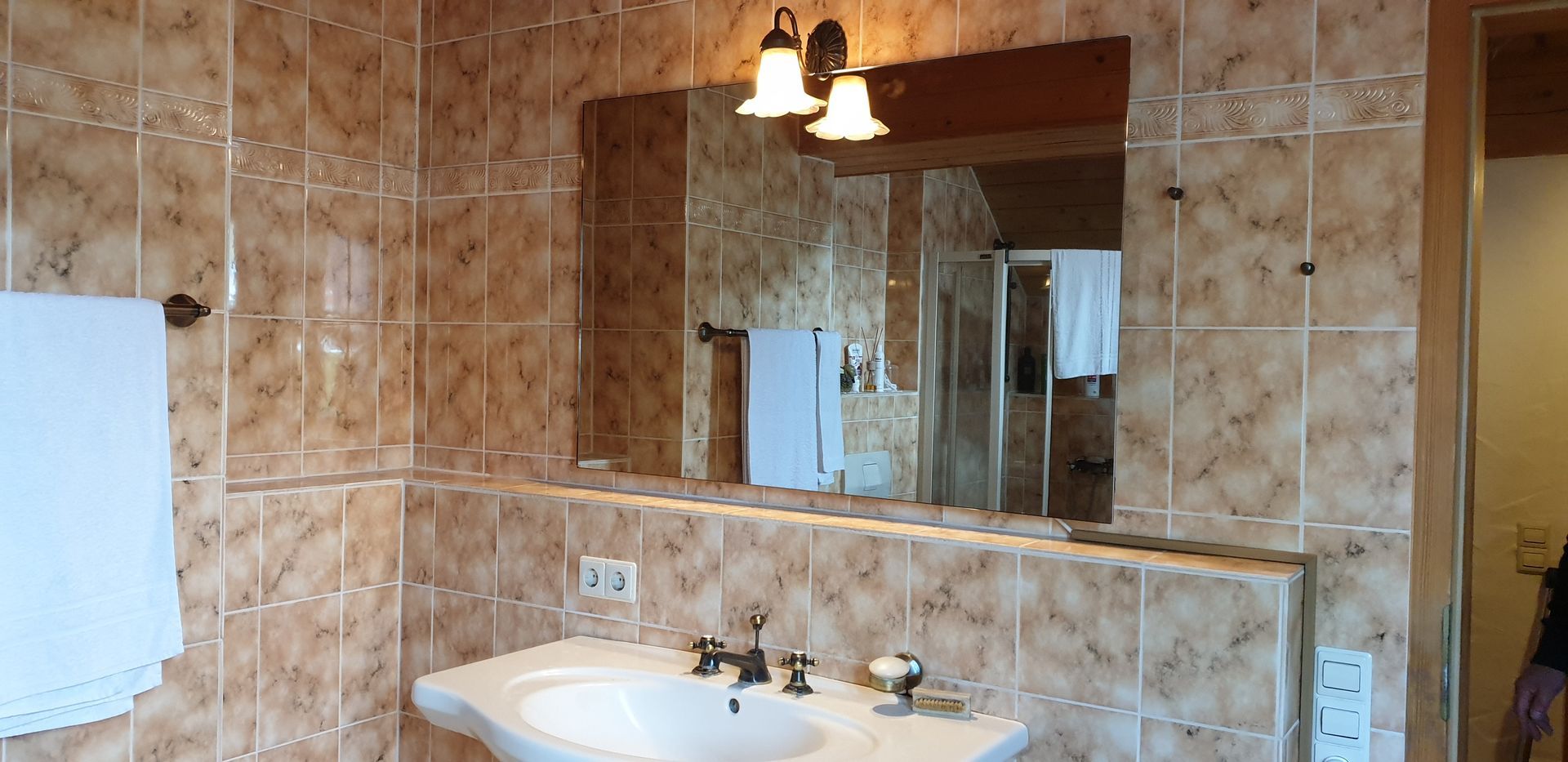 Gefliestes Badezimmer mit Waschbecken, Spiegel, Handtuchhalter und Duschkabine