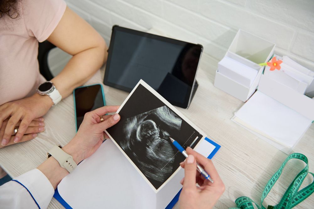 A pregnant woman is sitting at a table with a doctor looking at an ultrasound.