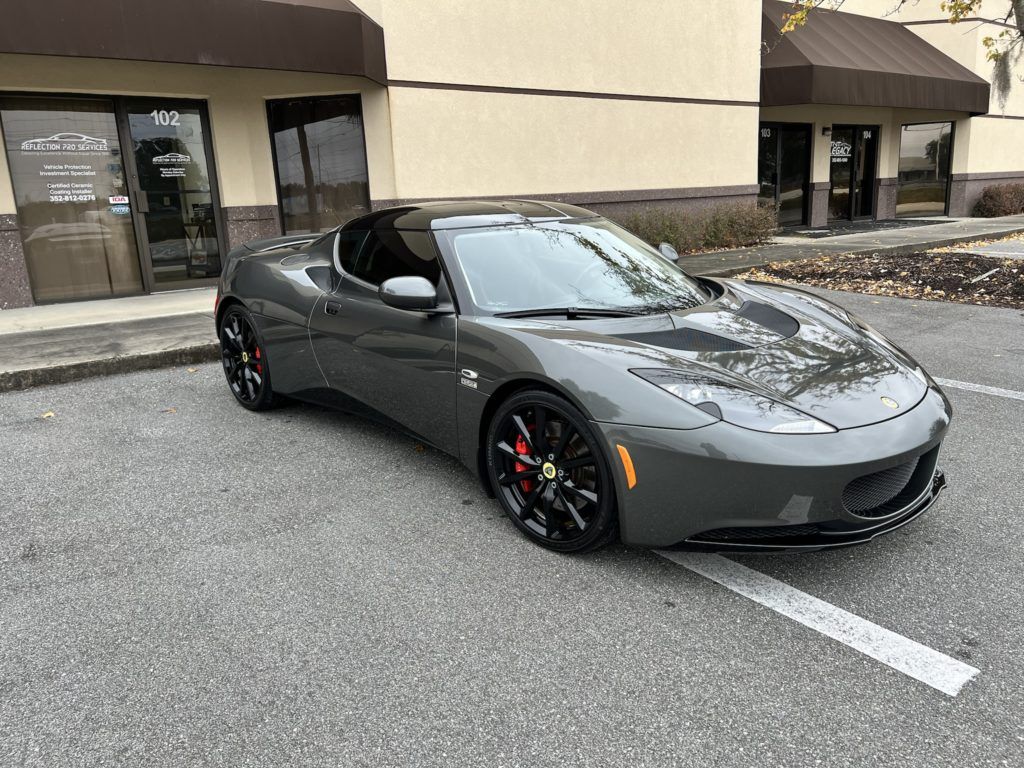 A gray sports car is parked in a parking lot in front of a building.