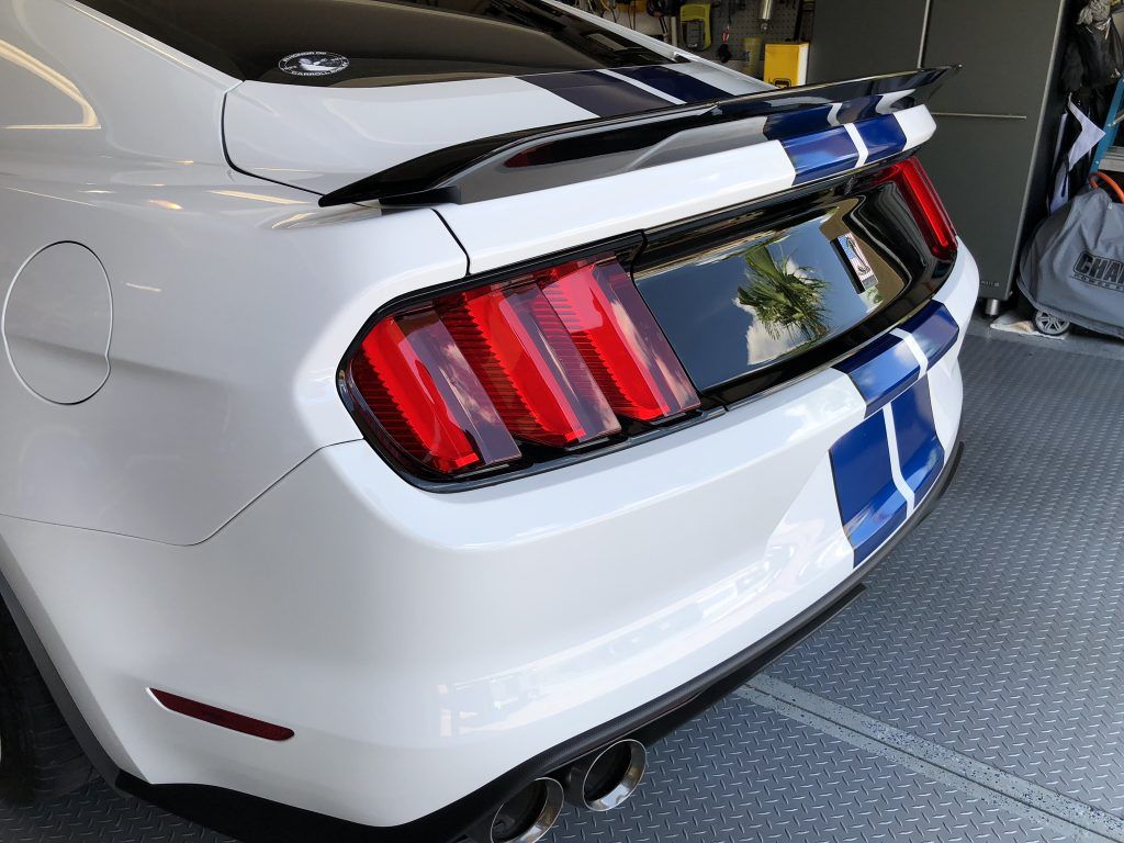A white mustang with blue stripes is parked in a garage.