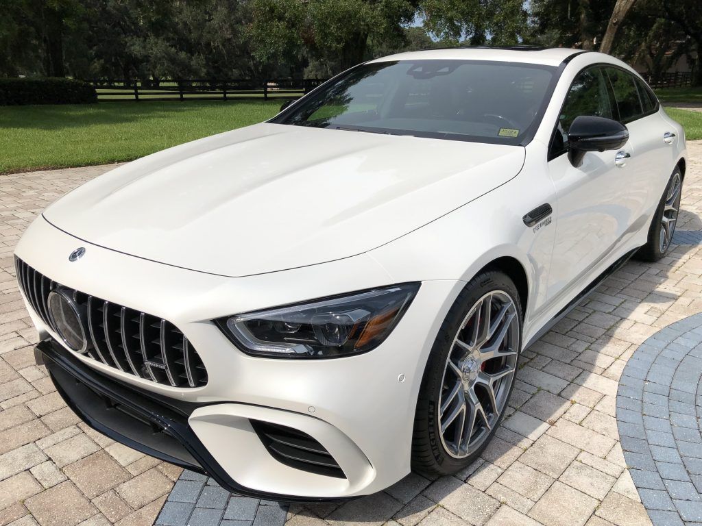 A white mercedes benz is parked on a brick driveway.
