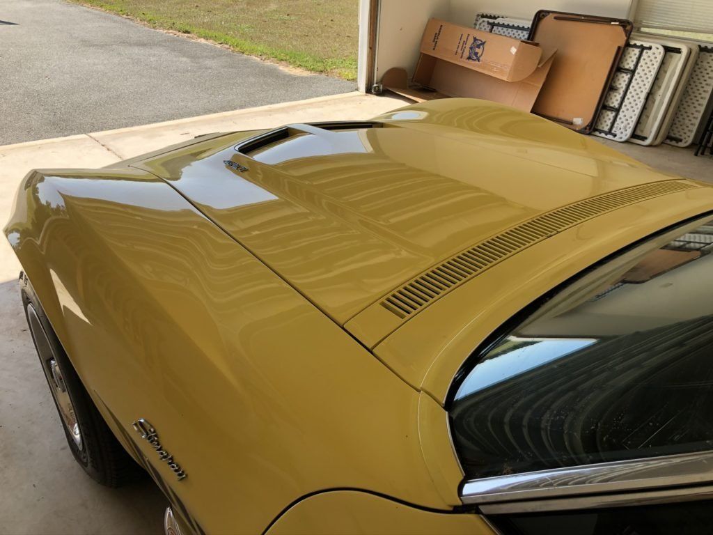 A yellow car is parked in a garage with the hood open