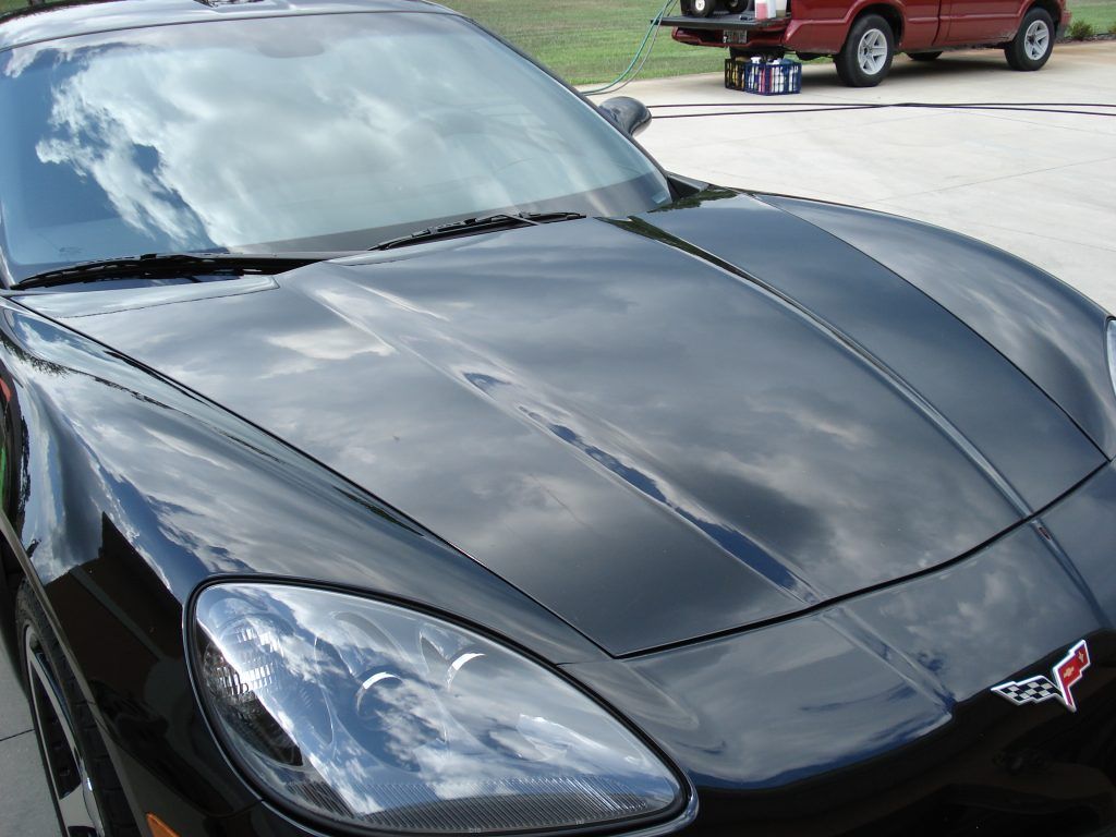 A black corvette is parked in a driveway next to a red truck