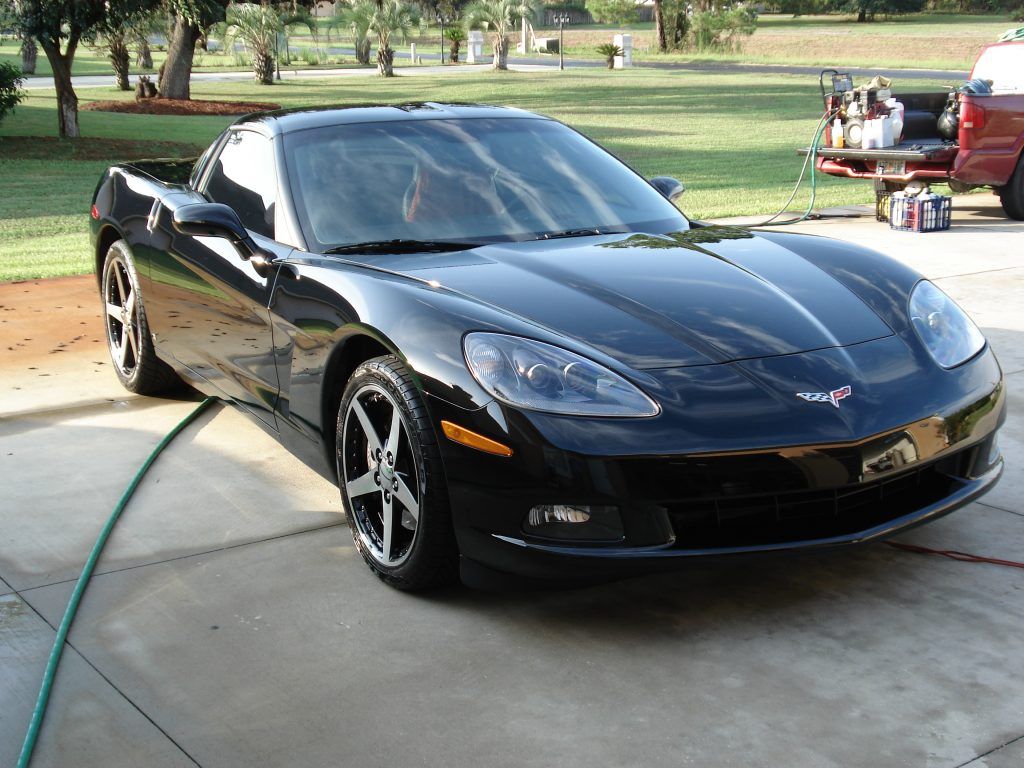 A black sports car is parked in a driveway next to a hose