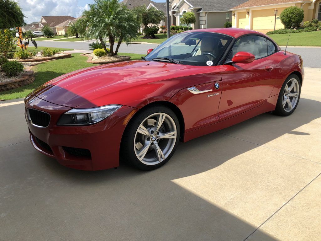 A red bmw z4 is parked in a driveway in front of a house.