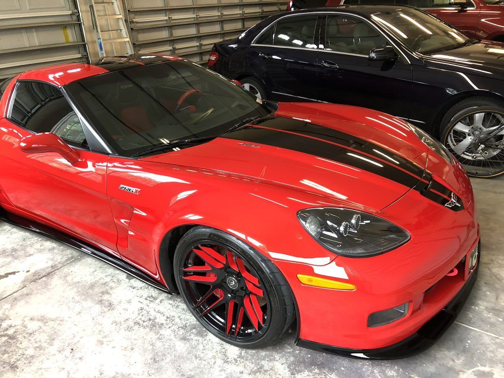 A red corvette is parked next to a black car in a garage.