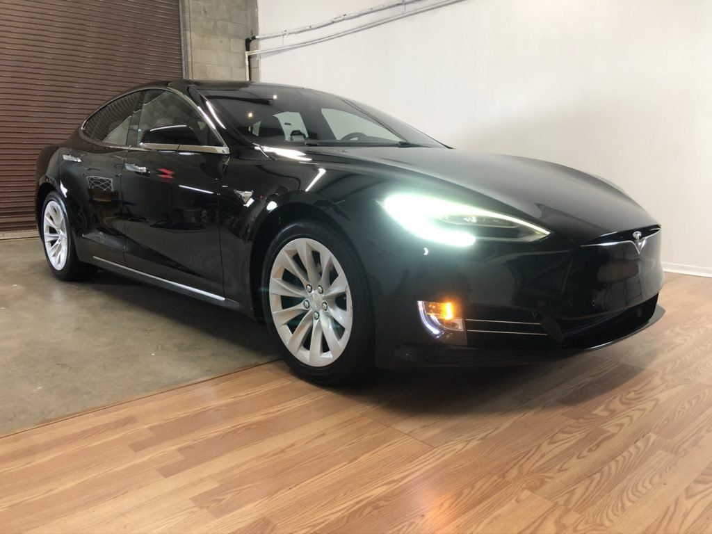 A black tesla model s is parked on a wooden floor in a garage.