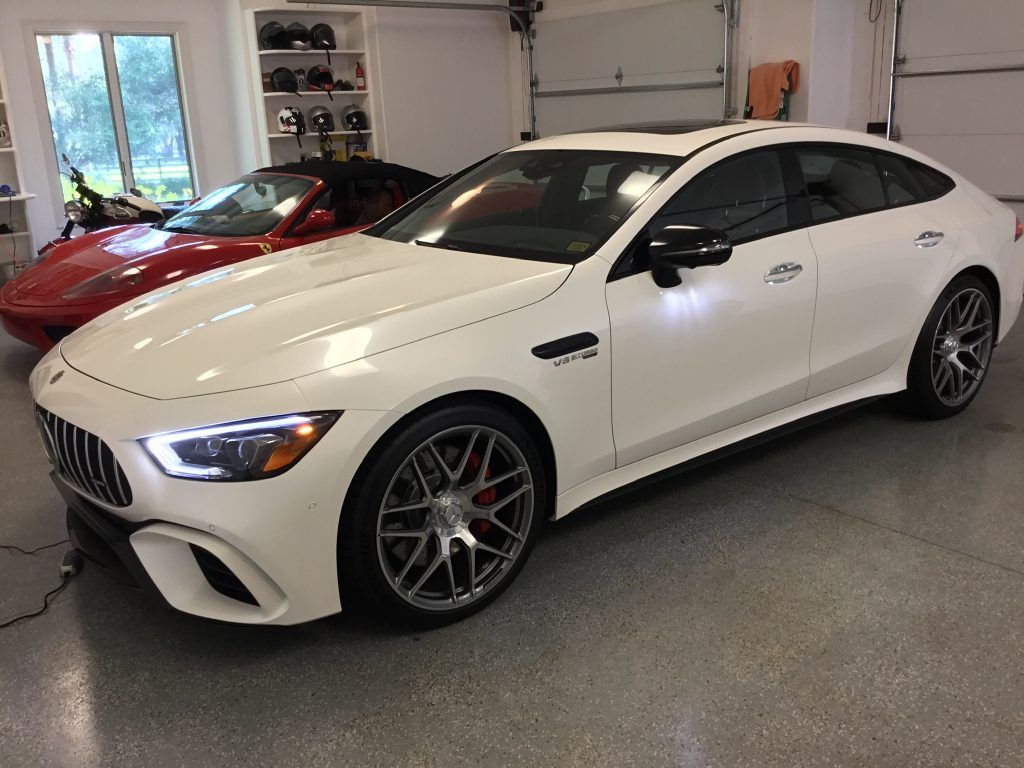 A white car is parked in a garage next to a red car.